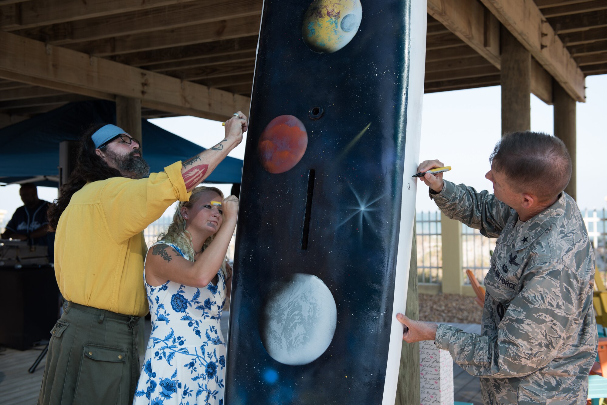 Brig. Gen. Wayne Monteith, 45th Space Wing commander, Sierra Gill and Duke Fortesque sign a sailboard during the 45th Space Wing’s 25th Anniversary Celebration Nov. 10, 2016, at the Beach House at Patrick Air Force Base, Fla. Gill and Fortesque used their artistic skills to create a sailboard symbolizing the wing’s storied history as the World’s Premier Gateway to Space. (U.S. Air Force photo by Matthew Jurgens) 