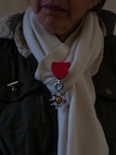 A woman awaits for the wreath laying ceremony to begin at the Lorraine American Cemetery to honor the deceased war veterans Nov. 11, 2016, at St. Avold, France. Pinned to her scarf is her deceased husband’s Legion of Merit medal, awarded to U.S. servicemembers for exceptionally meritorious conduct in the performance of outstanding services and achievements. Veteran’s Day is observed annually on November 11 and commemorates military veterans who currently serve or have served the U.S. armed forces, including those who gave the ultimate sacrifice. According to the DoD and Veterans Administration, since World War I, approximately 624,000 U.S. servicemembers have been killed in action battling in wars and conflicts. The Lorraine American Cemetery contains the buried remains of over 10,000 of them. It is the largest burial site of U.S. servicemembers in Europe. (U.S. Air Force photo by Airman 1st Class Lane T. Plummer)