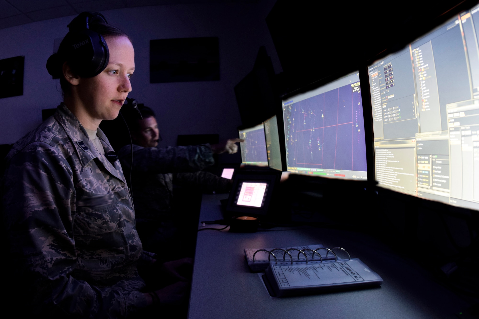 The faces of Capt. Jennifer and Maj. Michael (last names not used in accordance with Air Combat Command directives), 752nd Operation Support Squadron air battle managers, are illuminated by the glow of their computer screens as they follow and point out target aircraft during a training scenario on the AN/TYQ-23A emulator Oct. 31, 2016, Tinker Air Force Base, Okla. The trainees are working as part of a larger crew to test the communication and decision making skills of the individuals and team under a stressful environment. (Photos taken of systems configured to unclassified status by subject matter experts. Photo has been manipulated to blur the names of individuals shown.)(U.S. Air Force photo/Greg L. Davis)