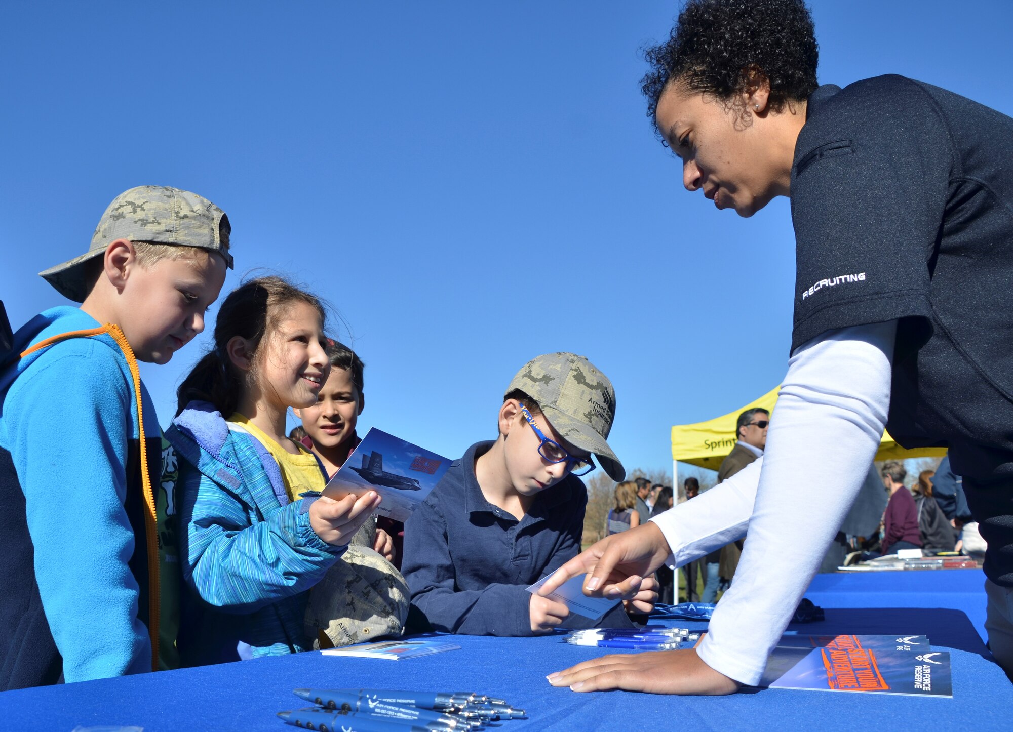 Tech. Sgt. Jessica Harrell, a 442d Fighter Wing recruiter, talks with kids as they look at Air Force Reserve post cards during the Veterans Day Celebration on Sprint Campus' Paige Field Nov. 10, 2016. Thousands of service members, veterans and community members gathered at the event to thank veterans and learn more about the military including National Guard and Reserve components. (U.S. Air Force photo/Senior Airman Missy Sterling)