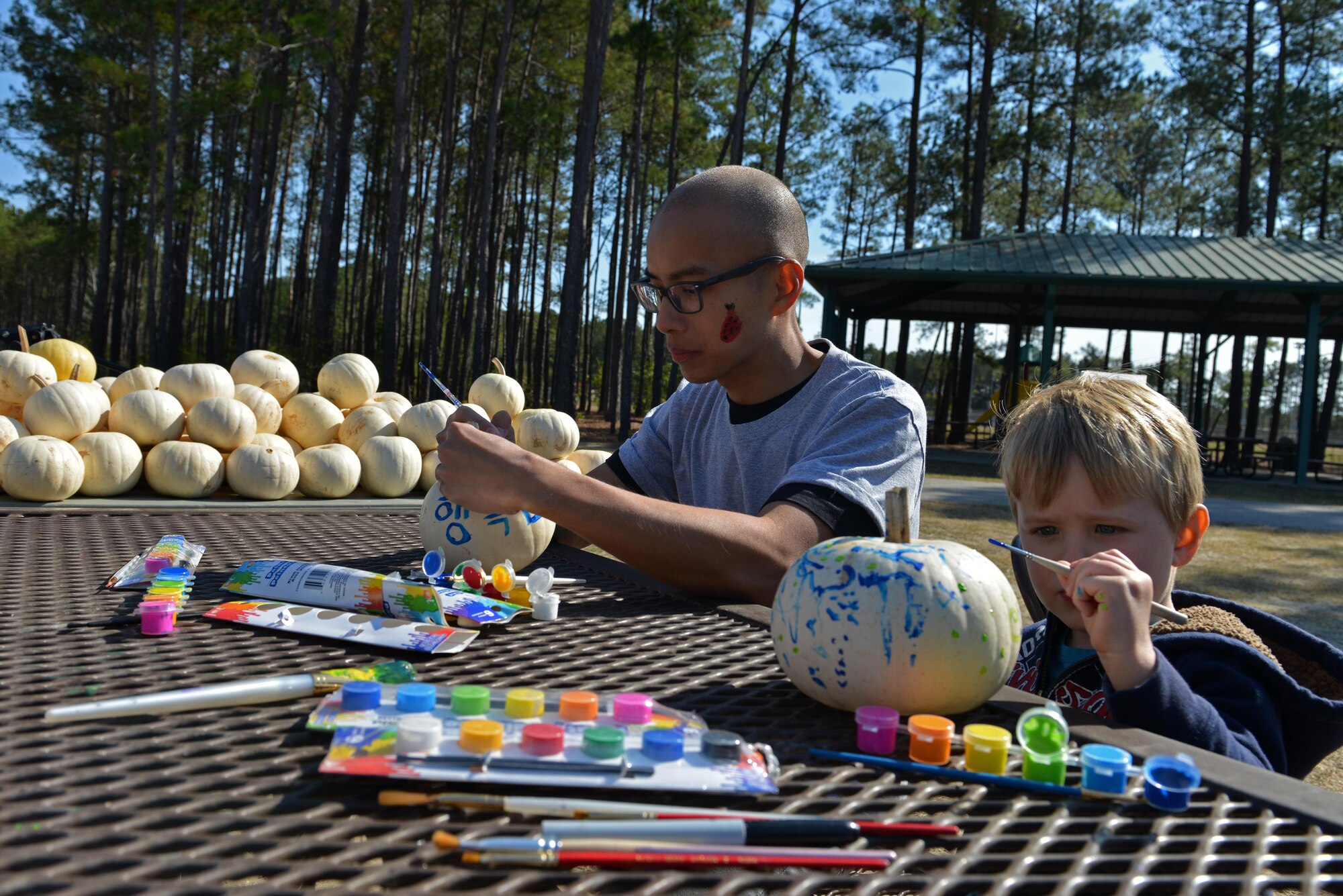 U.S. Air Force Senior Airman Andrew Verde, 20th Operational Weather Squadron weather forecaster, paints pumpkins with a child during a Team Shaw Fall Family Picnic at Shaw Air Force Base, S.C., Nov. 12, 2016. The picnic brought Airmen, Soldiers and their families together for a day of festivities and free food. (U.S. Air Force photo by Airman 1st Class Destinee Sweeney)