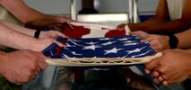 Maxwell honor guard members hold the American flag over a casket as its being ceremoniously folded during training with the Air Force Honor Guard Mobile Training Team, Nov. 9, 2016, Maxwell Air Force Base, Ala. The Air Force Honor Guard Mobile Training Team travels to Air Force bases across the United States and the world to ensure the standards are equal among all base honor guard teams. (U.S. Air Force photo/ Senior Airman Alexa Culbert)