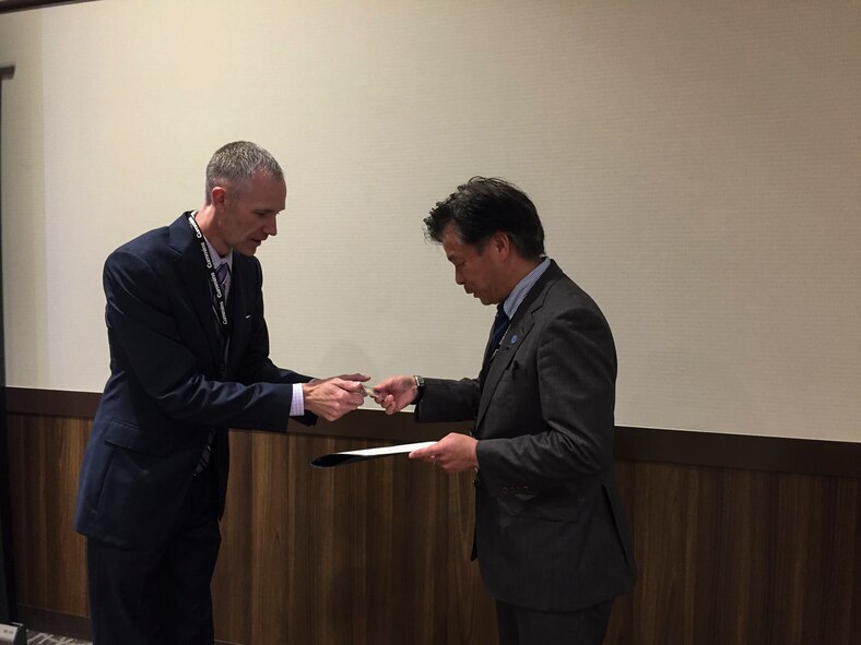 U.S. Air Force Col. Robert Grainger, 18th Civil Engineer Group commander, presents a Society of American Military Engineers coin to Takeya Kawamura, Japan Society of Professional Engineers president, during the SAME Japan Post symposium Nov. 7, 2016, in Okinawa, Japan. Engineering leaders from both the military and local community present the latest engineering information at different meetings held by SAME Japan Post. (U.S. Air Force photo by Senior Airman Lynette M. Rolen/Released)