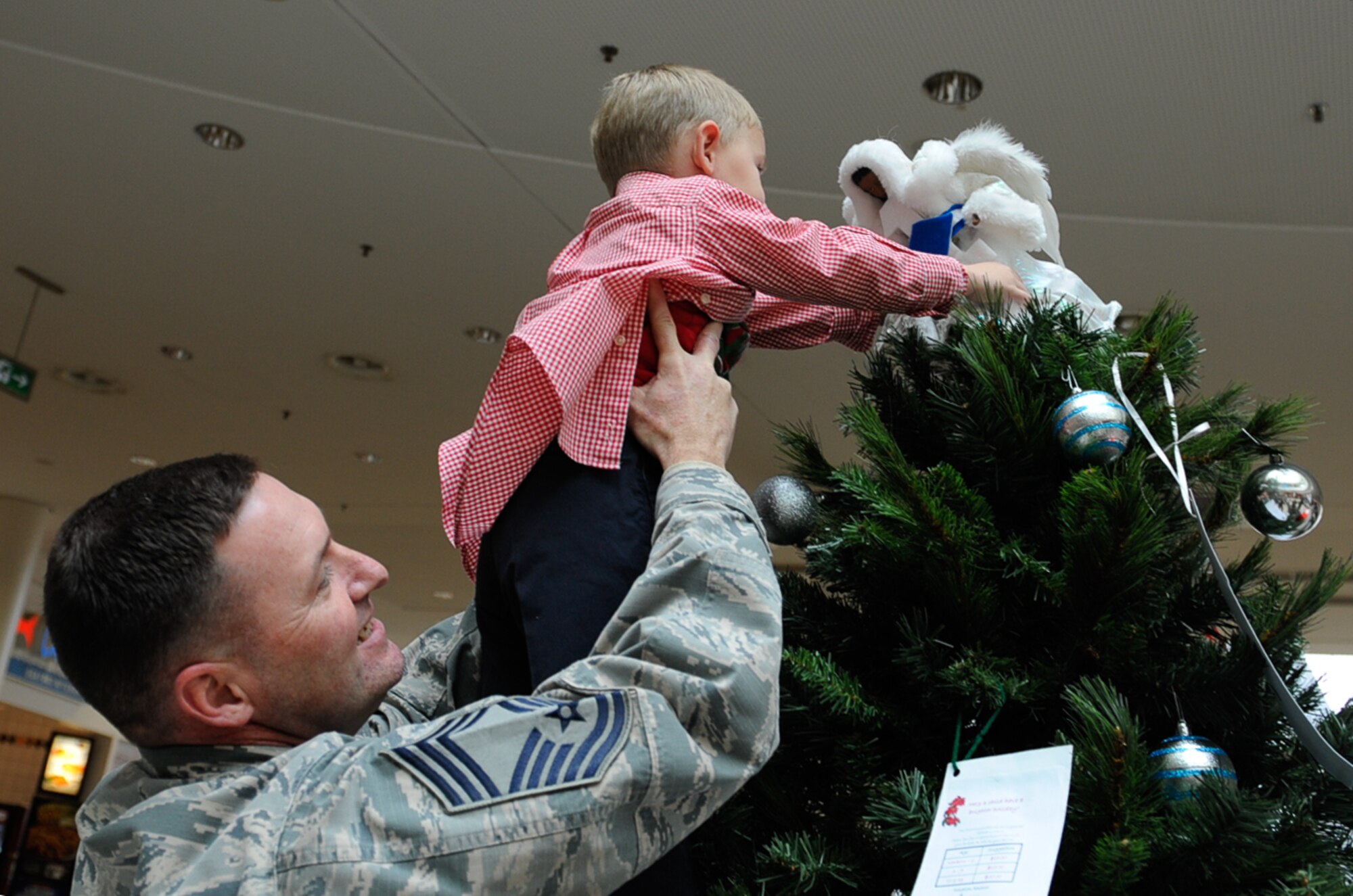 Chief Master Sgt. Taylor Jacobs, 21st Operational Weather Squadron superintendent, lifts his son, Wyatt Jacobs, to place an angel on a tree during the Angel Tree 2016 ceremony at Ramstein Air Base, Germany, Nov. 8, 2016. The Angel Tree program is an outreach program ran by first sergeants that provides monetary assistance to Airmen and their families, year-round. (U.S. Air Force photo by Airman 1st Class Savannah L. Waters)