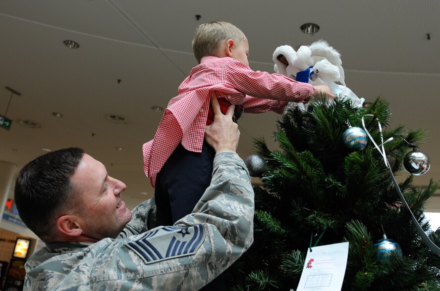 Chief Master Sgt. Taylor Jacobs, 21st Operational Weather Squadron superintendent, lifts his son, Wyatt Jacobs, to place an angel on a tree during the Angel Tree 2016 ceremony at Ramstein Air Base, Germany, Nov. 8, 2016. The Angel Tree program is an outreach program ran by first sergeants that provides monetary assistance to Airmen and their families, year-round. (U.S. Air Force photo by Airman 1st Class Savannah L. Waters)