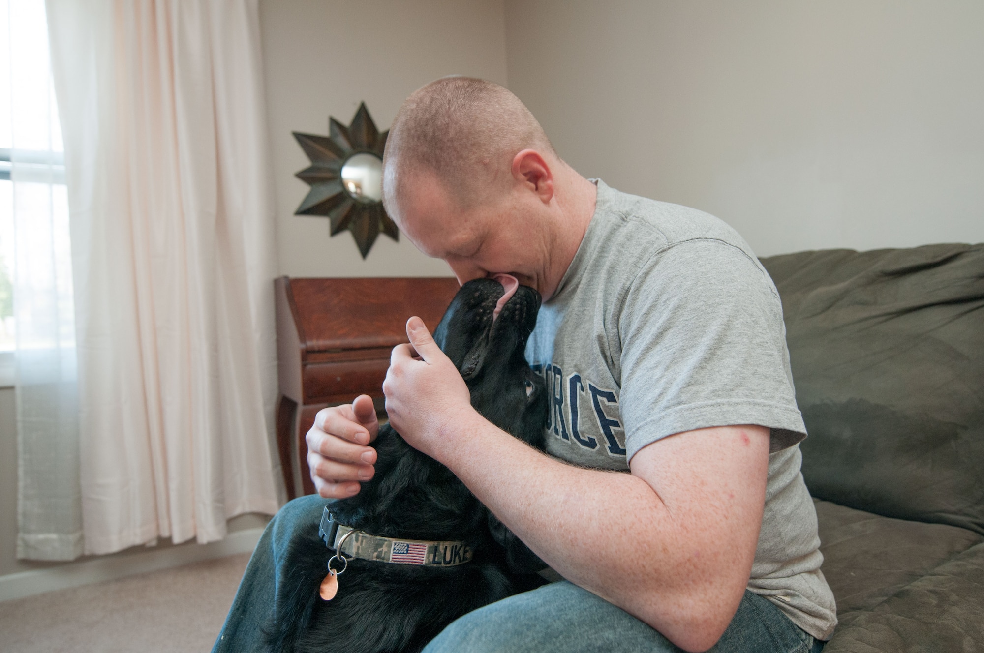 Staff Sgt. Ryan Garrison embraces his service dog Luke at their home in Glen Burnie, Md., March 29, 2016. Garrison, who works at the Defense Courier Station-Baltimore on Fort Meade, Md., recently received the Labrador who helps him cope with the physical and emotional effects of his combat-related injury. (U.S. Air Force photo/Sean Kimmons)