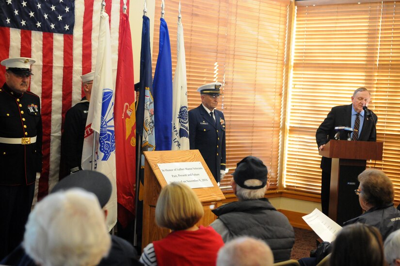 WAUWATOSA, Wisconsin (November 9, 2016) – Members of the Milwaukee NCO Council stand behind their respective service flag at the unveiling of the Veterans Memorial at Luther Manor, November 9, while retired Army Master Sgt. David Myers speaks during the ceremony. The memorial honors the more than 120 veteran residents of Luther Manor as well as all those that have and will live there.