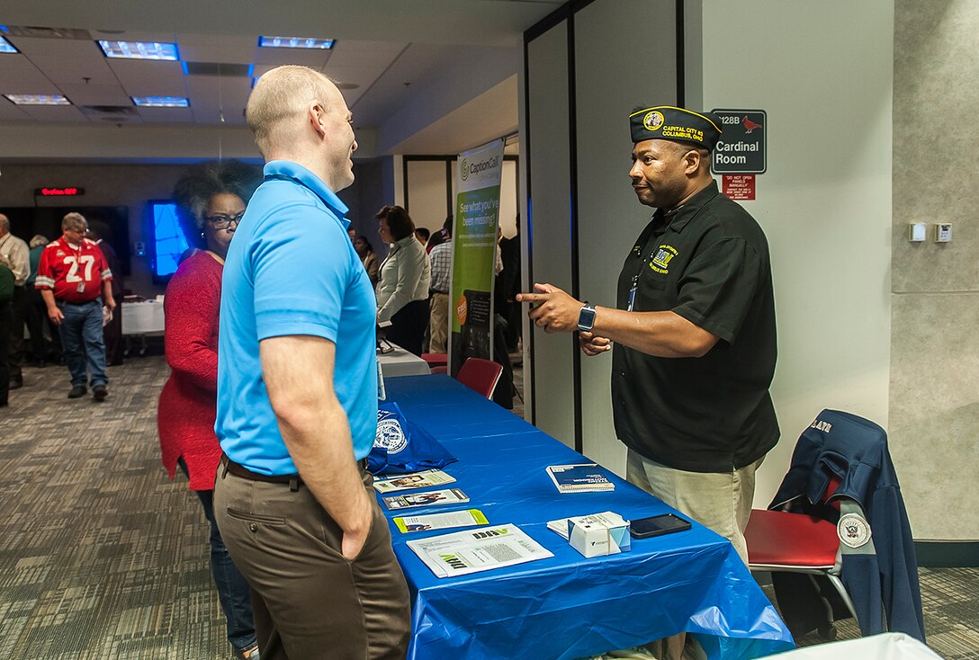 A representative from the Disabled American Veterans talks to a DSCC associate about what the charity offers during a Veterans Benefits fair Nov. 9 inside the DLA land and Maritime Operations Center. The fair was held in conjunction with the DSCC Veterans Day Program. 