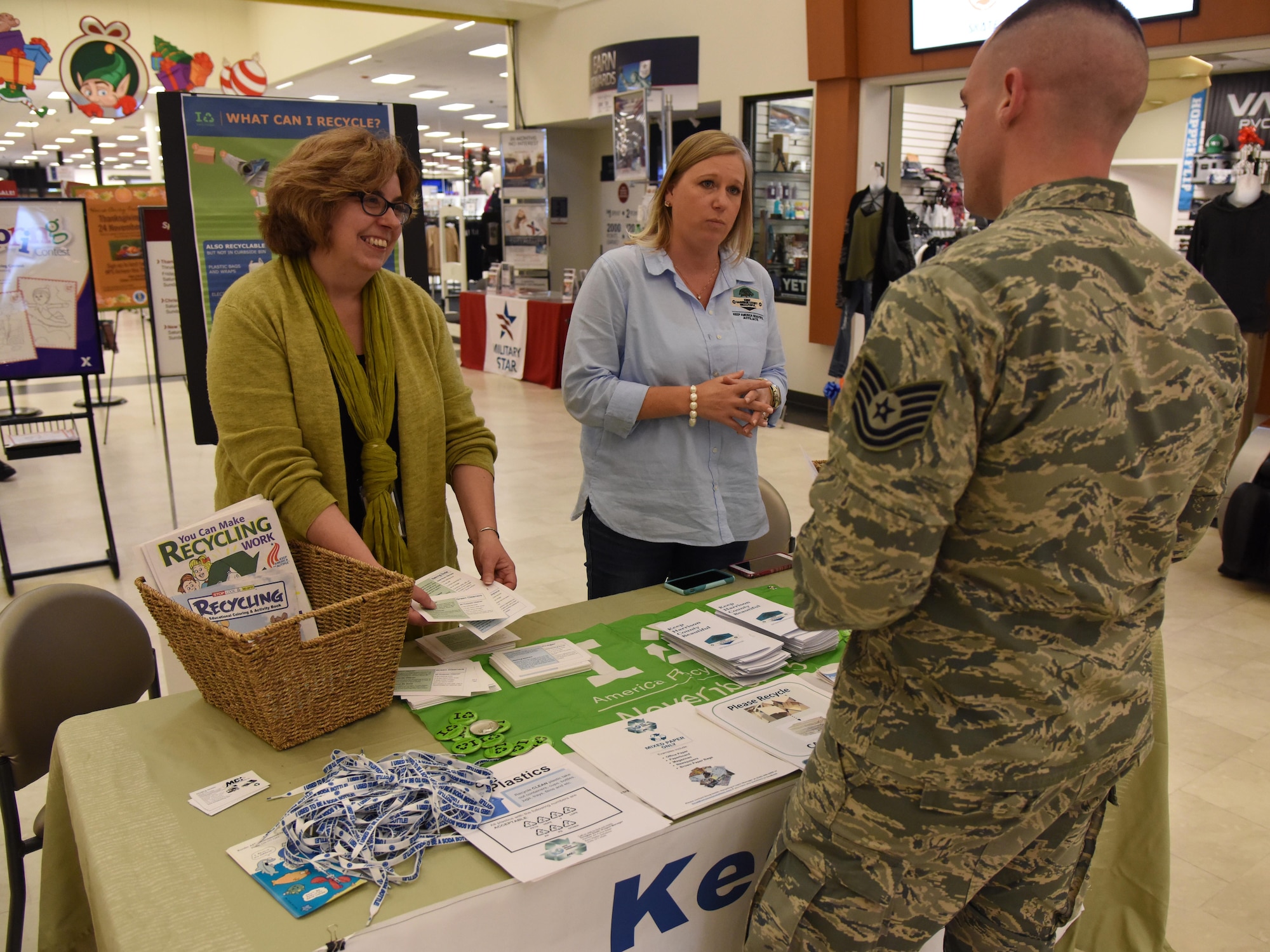 Susan Chamberlain, Base Operations Support community planner, and Kelly Griffin, Harrison County beautification director, provide educational recycling material to Tech. Sgt. Dayton Riter, 2nd Air Force executive assistant, at an American Recycling Day booth in The Exchange Nov. 15, 2016, on Keesler Air Force Base, Miss. Members of the base environmental office, recycling center and Harrison County Beautification Commission worked together to provide shoppers information about recycling. (U.S. Air Force photo by Kemberly Groue)
