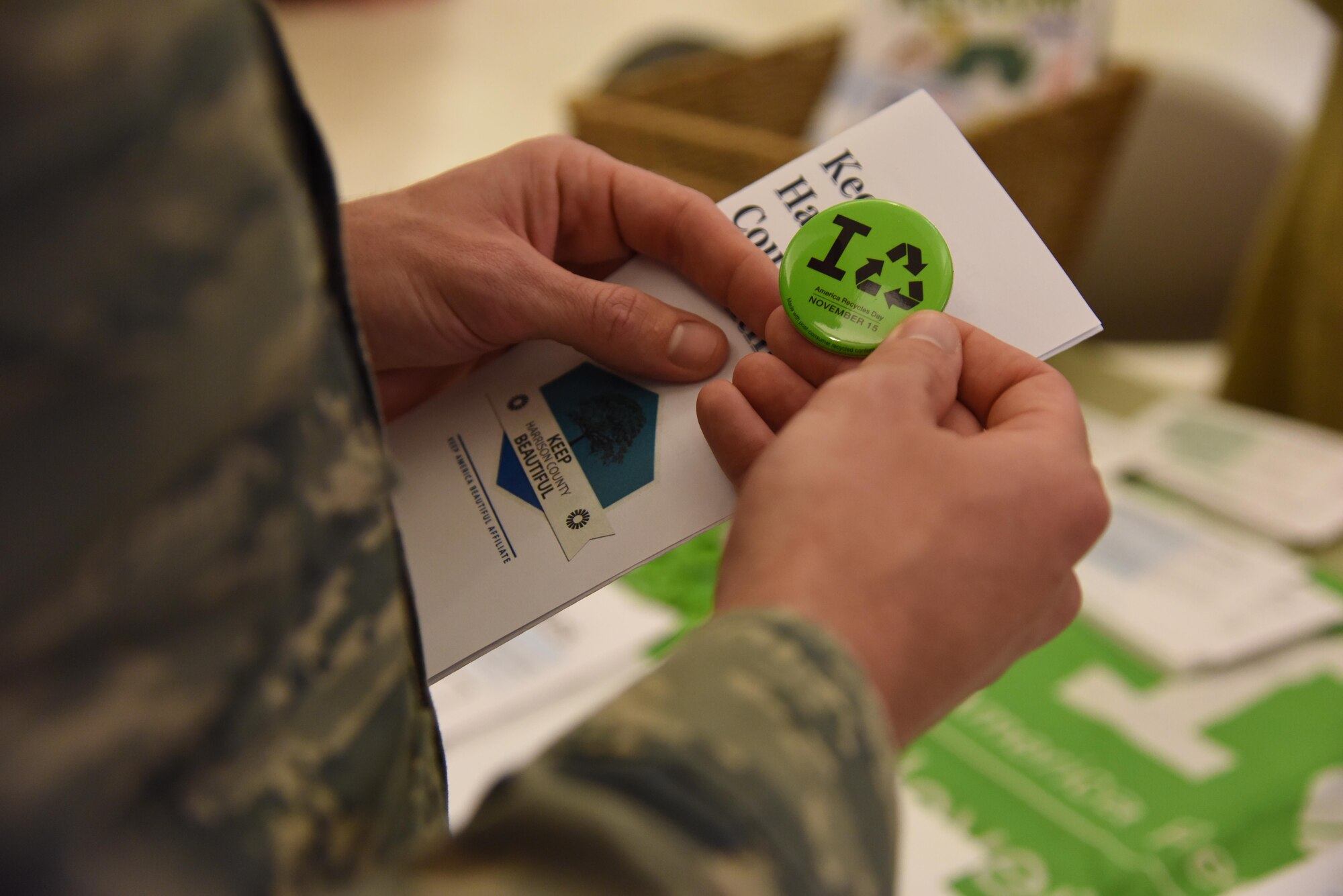 Tech. Sgt. Dayton Riter, 2nd Air Force executive assistant, holds an “America Recycles Day” pin at an American Recycling Day booth in The Exchange Nov. 15, 2016, on Keesler Air Force Base, Miss. Members of the base environmental office, recycling center and Harrison County Beautification Commission worked together to provide shoppers information about recycling. (U.S. Air Force photo by Kemberly Groue)