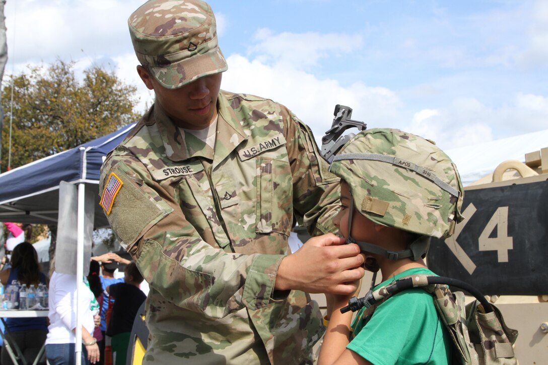 SAN ANTONIO- Spc. Isaiah Strouse, M2 Bradley Fighting Vehicle Crewman with Bravo Company 2-5 Cavalry, assists Dillon Kayastha with donning combat gear at the 1st Cavalry exhibit during the ‘Army vs. Irish’ football game November 12, 2016.  Dillon Kayastha, a New York native, joins his parents in support of the US Military Academy at West Point football team. (Photo by Army Reserve Sgt. Zechariah Gerhard, 345th Public Affairs Detachment)