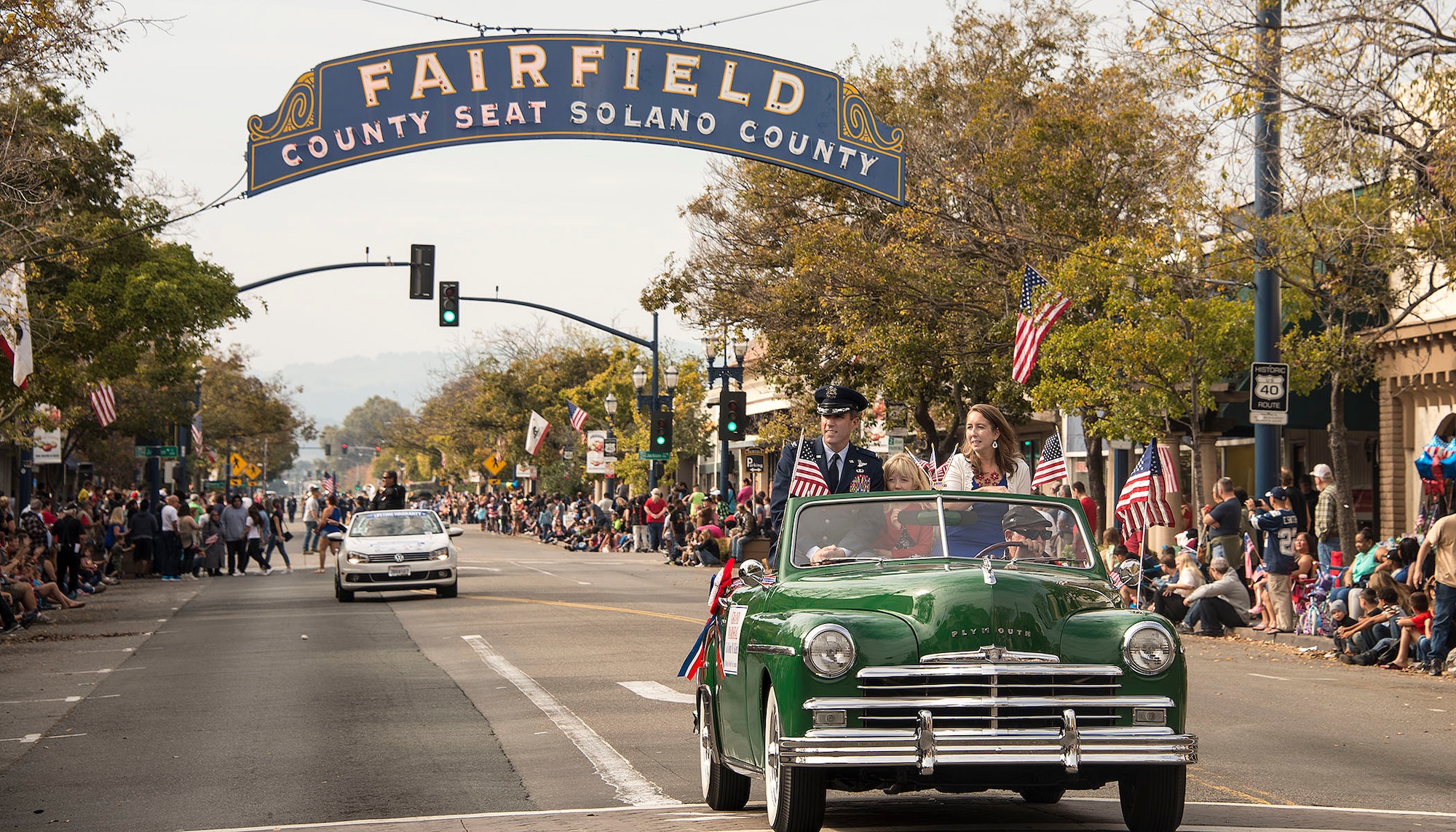 Col. John Klein Jr., 60th Air Mobility Wing commander, and his wife and daughter wave to cheering crowds as they ride through downtown Fairfield, Calif, during the town’s annual Veterans Day Parade Nov. 11, 2016. Klein was the grand marshal of the parade, which lasted two-and-a-half hours with over 70 entries.   (U.S. Air Force Photo by T.C. Perkins Jr.)
