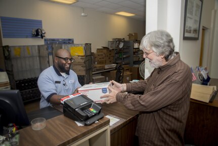Kenneth Collins (left), United States Postal Services sales and services associate, receives a package from Joe Beach, 502nd Air Base Wing Public Affairs graphic artist, Nov. 15 at the Joint Base San Antonio-Randolph Post Office. The holiday rush at U.S. Postal Service locations is near at hand, so it’s advisable for the families of active-duty members who are serving abroad to mail cards, letters and packages to their loved ones as soon as possible.