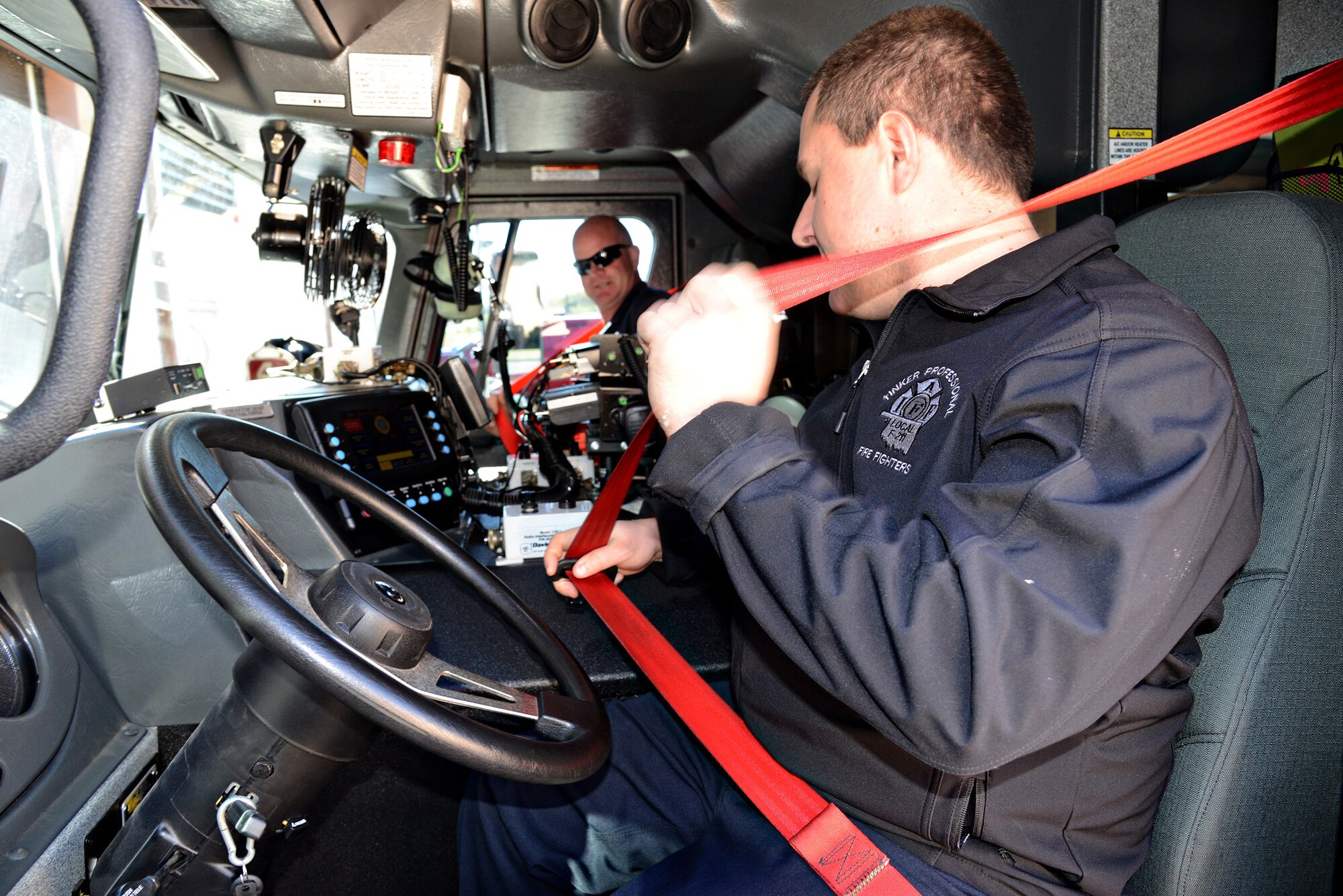 Lt. Justin Fordyce, front, and Lt. Vince Dill, demonstrate the seatbelt safety system in fire truck 4. The crews on each truck have a friendly competition going on with each other to receive the lowest amount of safety violations through the system. The system keeps everyone safe by alerting them if a seatbelt isn’t buckled, but the crews now hold each other accountable before a violation even occurs. (Air Force photo by Kelly White)