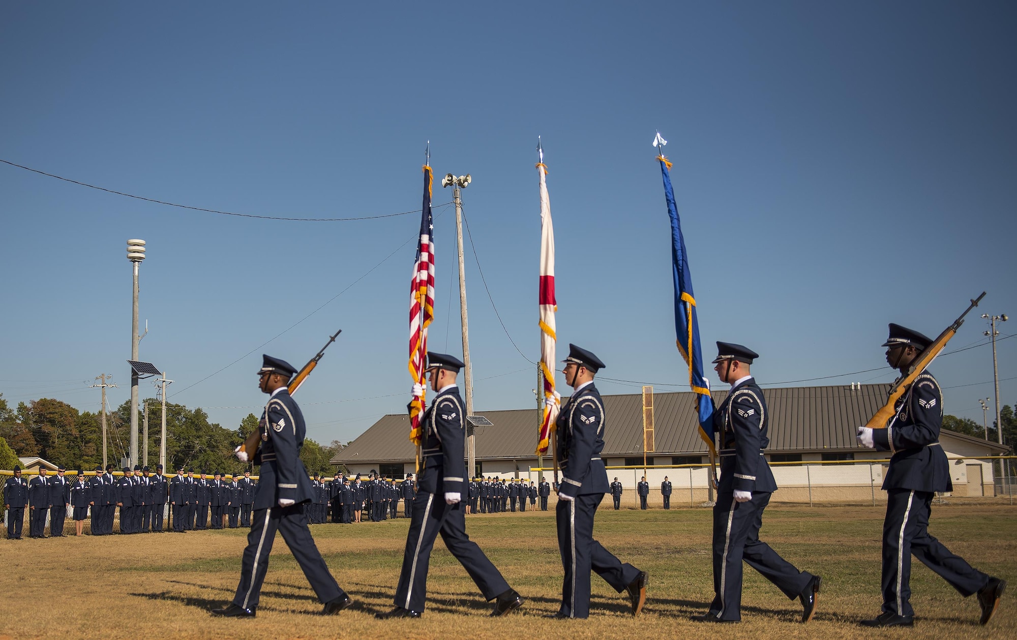 An Honor Guard team carries the colors by a line of Airmen waiting for their moment to enter the Community College of the Air Force graduation ceremony at Eglin Air Force Base, Fla., Nov. 16.  More than 300 Airmen from Eglin and Duke Field were honored at this year’s event. (U.S. Air Force photo/Samuel King Jr.)