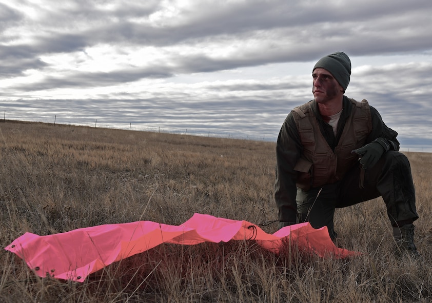 A pilot assigned to the 28th Bomb Wing, Ellsworth Air Force Base, S.D., waits for rescue at a simulated crash site near Belle Fourche, S.D., Nov. 16, 2016. The bright tarp laid out on the ground is a way to attract the attention of rescue pilots without drawing unwanted attention from hostile ground forces. (U.S. Air Force photo by Airman 1st Class James L. Miller) 