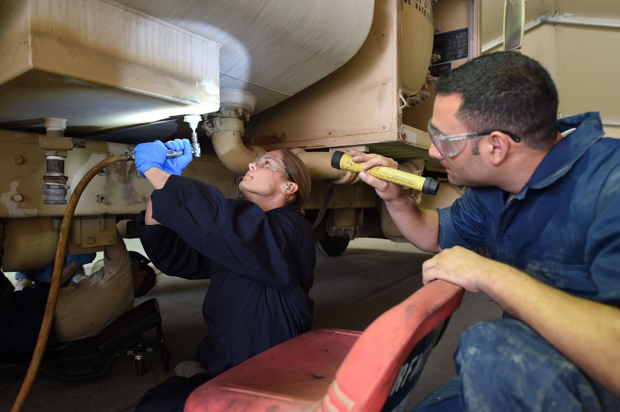 Senior Airman Johnathan, 380th Fire and Refueler Maintenance vehicle maintainer, directs a flashlight to the area of an R-11 fuel truck that Capt. Jennifer, 380th Air Expeditionary Wing executive officer, is grinding the paint off of at an undisclosed location in Southwest Asia, November 16, 2016. Col. Kevin Eastland, 380th AEW vice commander, and Jennifer joined the FARM members for applying a service kit to the tank sump on the last R-11 requiring the kit. (U.S. Air Force photo by Tech. Sgt. Christopher Carwile)