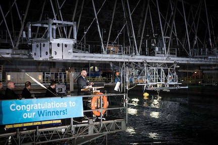 Alex Hagmuller, a mechanical engineer from the Portland, Oregon-based team AquaHarmonics, tells the crowd how their wave energy converter (WEC) is working to absorb energy from waves, which can then be converted and used as a power source. AquaHarmonics competed against eight other teams to win the 2016 Wave Energy Prize of $1.5 million, which was awarded Nov. 16 at Naval Surface Warfare Center, Carderock Division in West Bethesda, Md. The final testing stage took place at the Maneuvering and Seakeeping (MASK) Basin, Carderock's state-of-the-art indoor ocean. The Wave Energy Prize is a public prize competition sponsored by the U.S. Department of Energy (DoE), and supported by the Office of Naval Research (ONR) and Carderock. (U.S. Navy photo by Monica McCoy/Released)