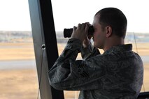 Senior Airman Erik Johnson, 5th Operations Support Squadron air traffic controller, looks through binoculars from the control tower at Minot Air Force Base, N.D., Nov. 15, 2016. Johnson is checking for any ground obstructions and scanning the sky for birds to ensure aircraft safety during taxiing, take-off and landing. (U.S. Air Force photo/Senior Airman Kristoffer Kaubisch)