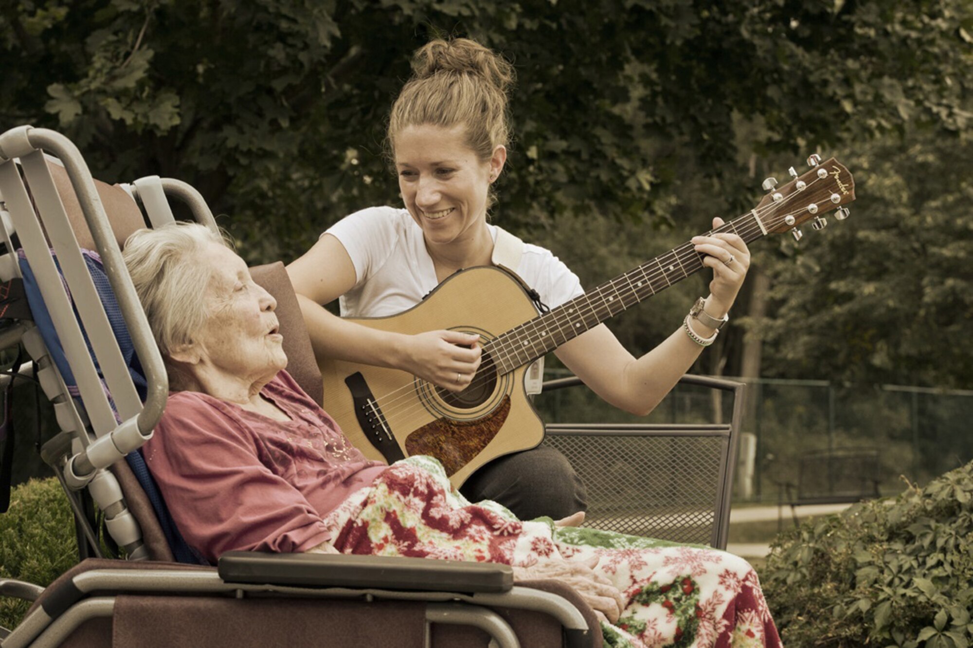 U.S. Air Force Staff Sgt. Carrie Gatz, an instrumentalist with the 566th Air Force Band, Illinois Air National Guard, plays guitar for a hospice patient at her civilian job Sept. 11, 2013. Gatz has served in the Air National Guard since 2004. (Photo © Bart Harris, used by permission.)