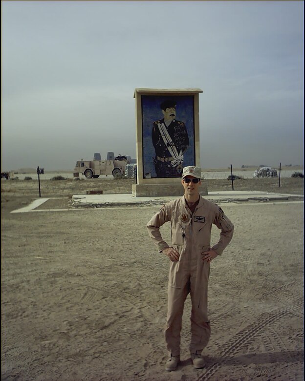 U.S. Air Force Maj. John Marks, 303rd Fighter Squadron pilot, poses in front of a Saddam sign near Tallil Air Base, Iraq, during Operation Iraqi Freedom in 2003. Other bases Marks has deployed to in support of Operation Iraqi Freedom include Ahmed Al Jaber AB, Kuwait, and Kirkuk AB, Iraq. (Courtesy photo provided by Lt. Col. Marks)