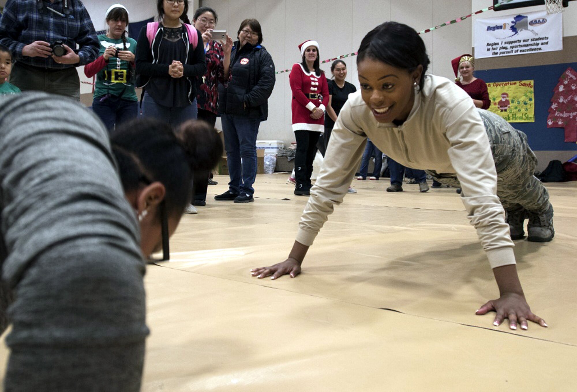 TOGIAK, Alaska -- Senior Airman Denise Barnes, with the Air Force Reserve's 55th Aerial Port Squadron, accepts a push-up challenge from a resident Nov. 15, 2016. Barnes was one of a handful of reservists who traveled from Travis Air Force Base, Calif., to assist with Operation Santa Claus 2016. Now in its 60th year, Operation Santa Claus is an Alaska National Guard-led program that delivers toys, school supplies and other gifts to children in Alaska's remote villages. (U.S. Air National Guard photo by Maj. John Callahan/released)
