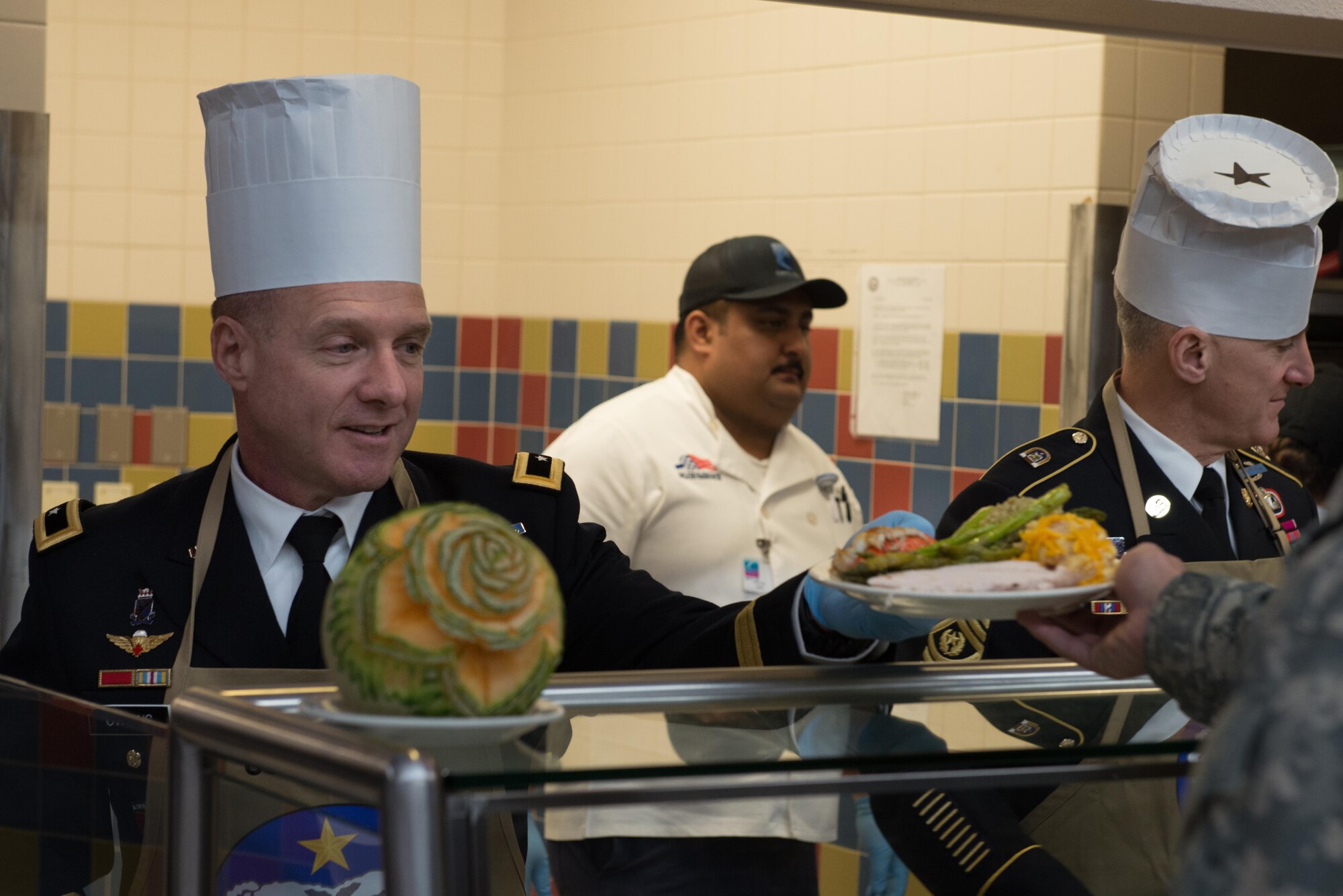 Army Maj. Gen. Bryan Owens, United States Army Alaska, Commander and USARAK Command Sgt. Maj Michael Ferrusi serve up a dish loaded with food to a Joint Base Elmendorf-Richardson Soldier Nov 23 at the Wilderness Inn Dining Facility. As a matter of tradition, every year, base leadership serve the Soldiers and Airmen of JBER a thanksgiving meal. 