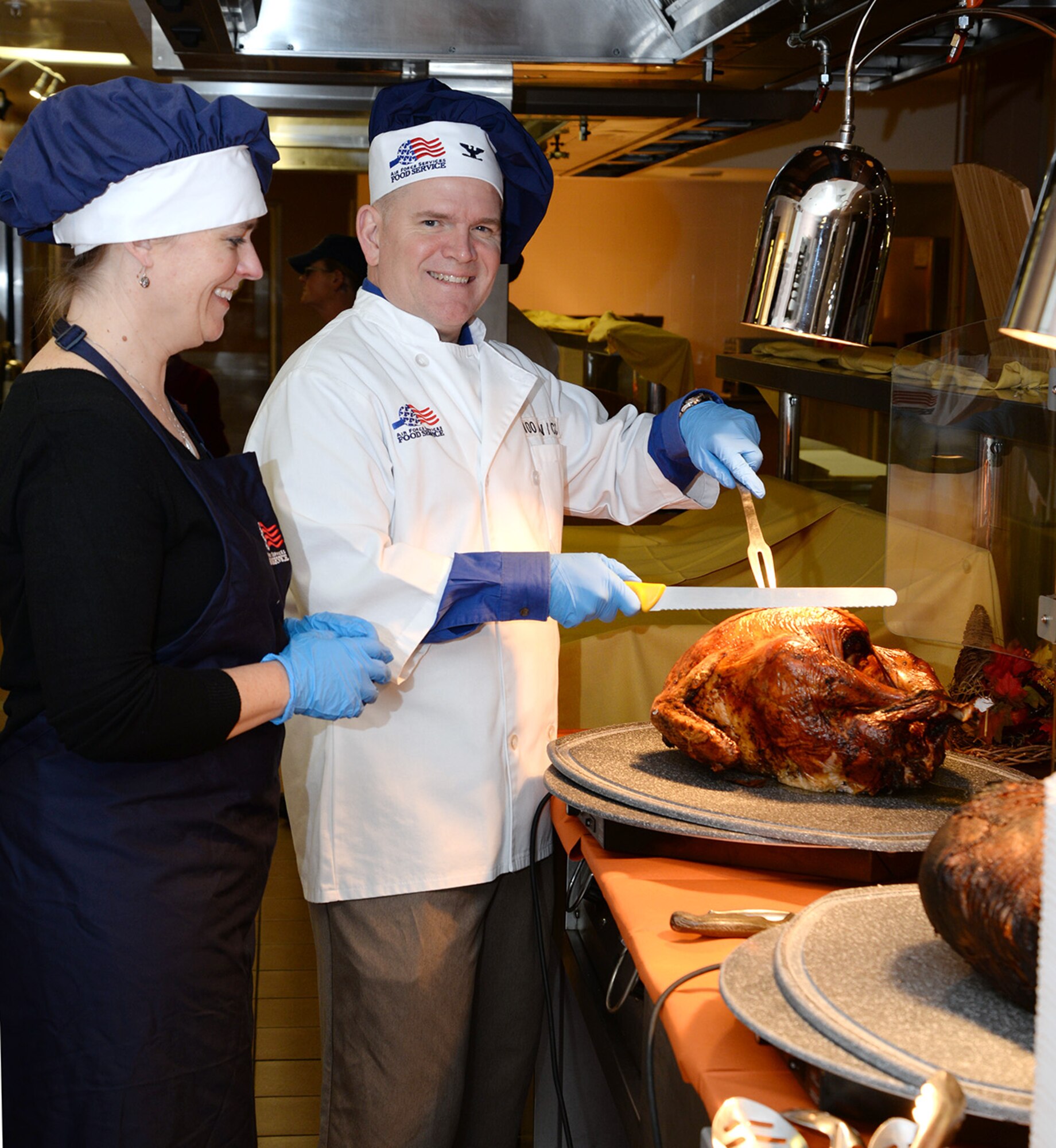 U.S. Air Force Col. Thomas D. Torkelson, right, 100th Air Refueling Wing commander, prepares to carve a turkey as his wife Debbie, left, stands by to help serve other food to customers Nov. 24, 2016, at the Gateway Dining Facility on RAF Mildenhall, England. Team Mildenhall leadership and spouses joined with the dining facility staff serving food to provide Airmen and civilians an opportunity to enjoy Thanksgiving lunch. (U.S. Air Force photo by Karen Abeyasekere)