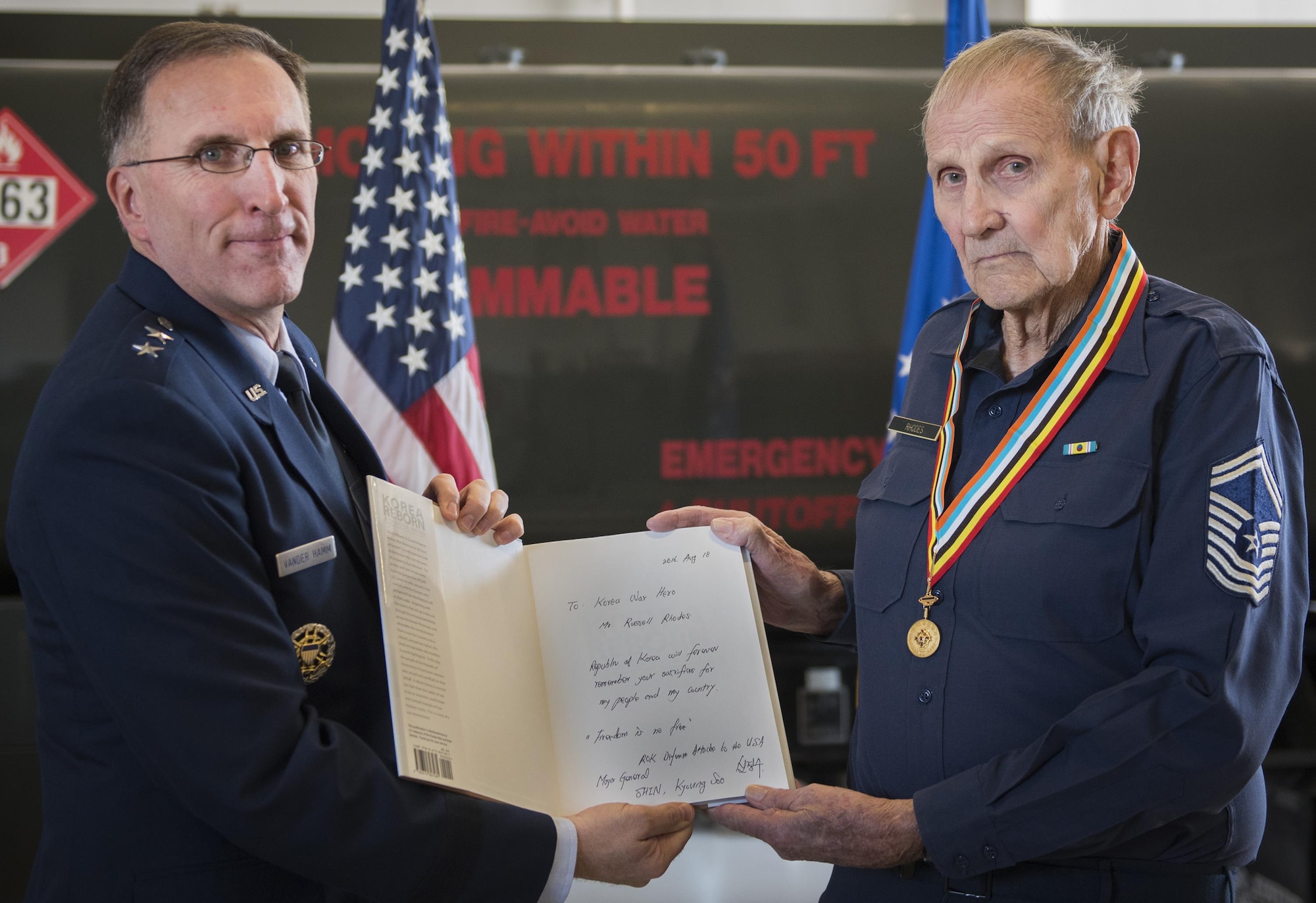 Maj. Gen. Scott Vander Hamm, the Air Force assistant deputy chief of staff of operations, holds a signed book with his uncle, retired Chief Master Sgt. Russell Rhodes, after presenting him with the Korean Ambassador for Peace Medal during a ceremony held at Eglin Air Force Base, Fla., Nov. 15, 2016. The 85-year-old Rhodes requested the medal ceremony be held at the base’s fuels flight, where Rhodes was stationed during his Air Force career as a fuel truck driver. (U.S. Air Force photo/Samuel King Jr.)