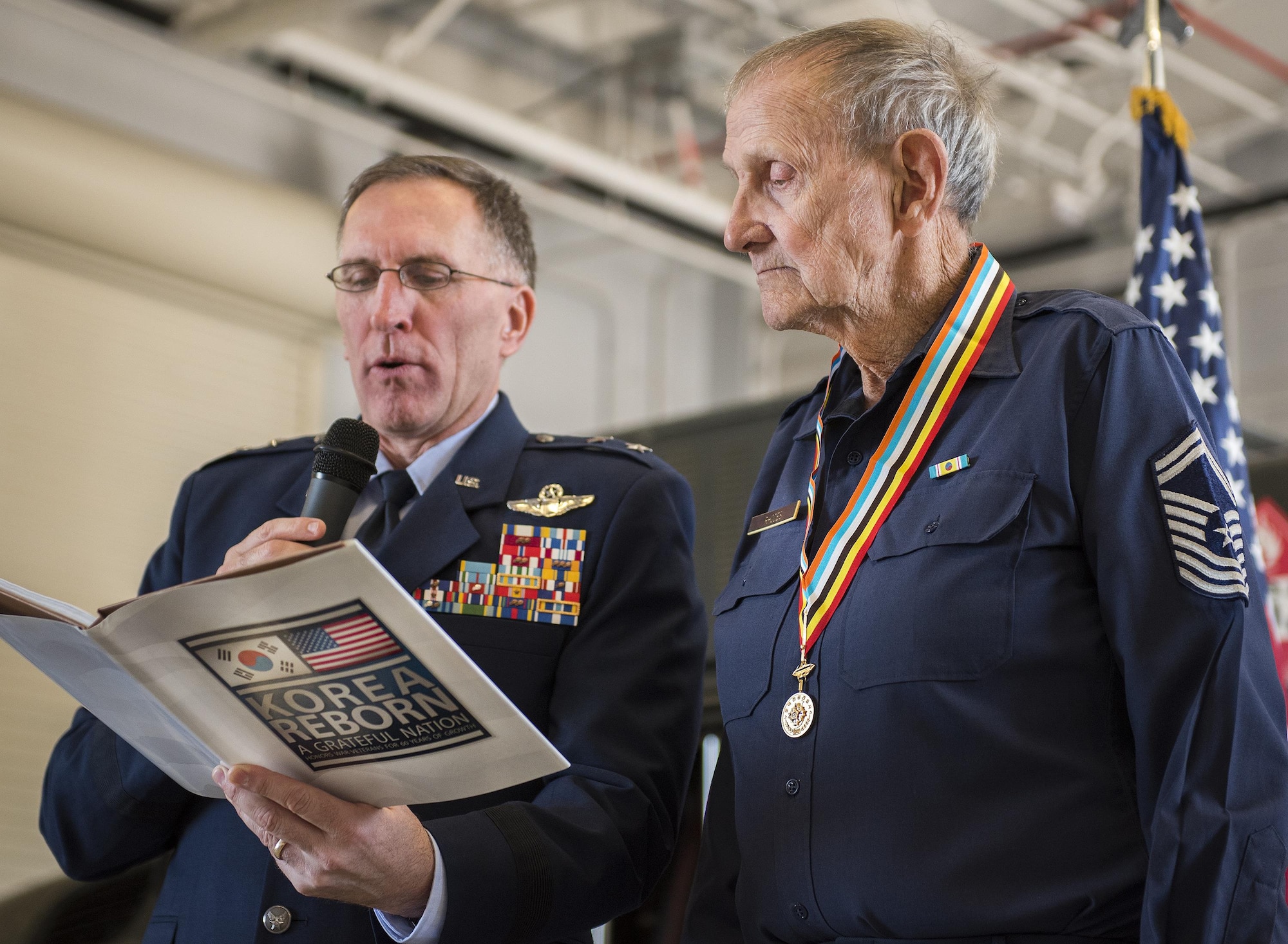 Maj. Gen. Scott Vander Hamm, the Air Force Assistant Deputy Chief of Staff, Operations, reads a book inscription for his uncle, retired Chief Master Sgt. Russell Rhodes, after presenting him with the Korean Ambassador for Peace Medal during a ceremony held at Eglin Air Force Base, Fla., Nov. 15.  The 85-year-old Rhodes requested the medal ceremony be held at the base’s fuels flight, where Rhodes was stationed during his Air Force career as a fuel truck driver.  (U.S. Air Force photo/Samuel King Jr.)