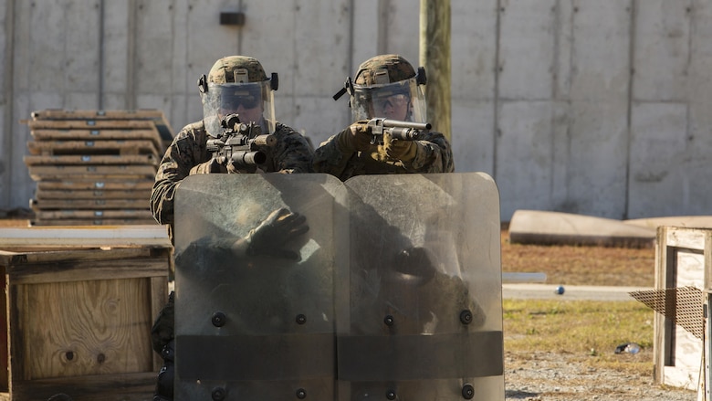 Marines, to the side of the shield line, provide notional cover during the final exercise of the non-lethal weapons training course at Camp Lejeune N.C., Nov. 18, 2016. Marines with 3rd Battalion, 6th Marine Regiment, 2nd Marine Division, participated in the training in preparation for their deployment with the 24th Marine Expeditionary Unit. 