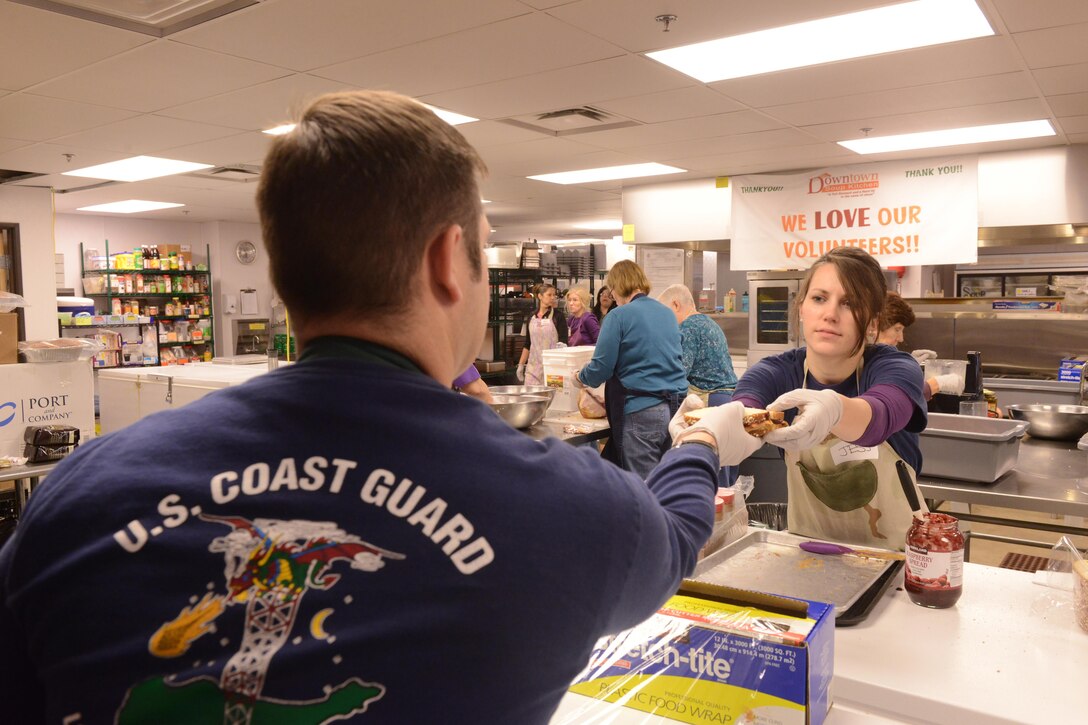 Coast Guard Lt. j.g. Jessica Stock passes a sandwich to Coast Guard Lt. j.g. Richard Sprouse while volunteering at the Downtown Soup Kitchen Hope Center in Anchorage, Alaska, Nov. 29, 2016. Stock and Sprouse are assigned to Coast Guard Sector Anchorage. Coast Guard photo by Petty Officer 1st Class Bill Colclough.
