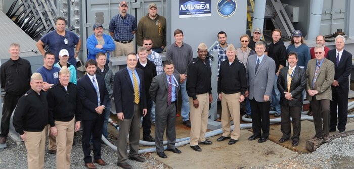 Vice Adm. Thomas Moore, commander of the Naval Sea Systems Command, center right, and Capt. Godfrey "Gus" Weekes, Naval Surface Warfare Center Dahlgren Division (NSWCDD) commanding officer, are pictured with their military and technical leadership - including the NSWCDD electromagnetic railgun team - in front of the electromagnetic railgun at the Potomac River Test Range during Moore's NSWCDD visit, Nov. 30. 