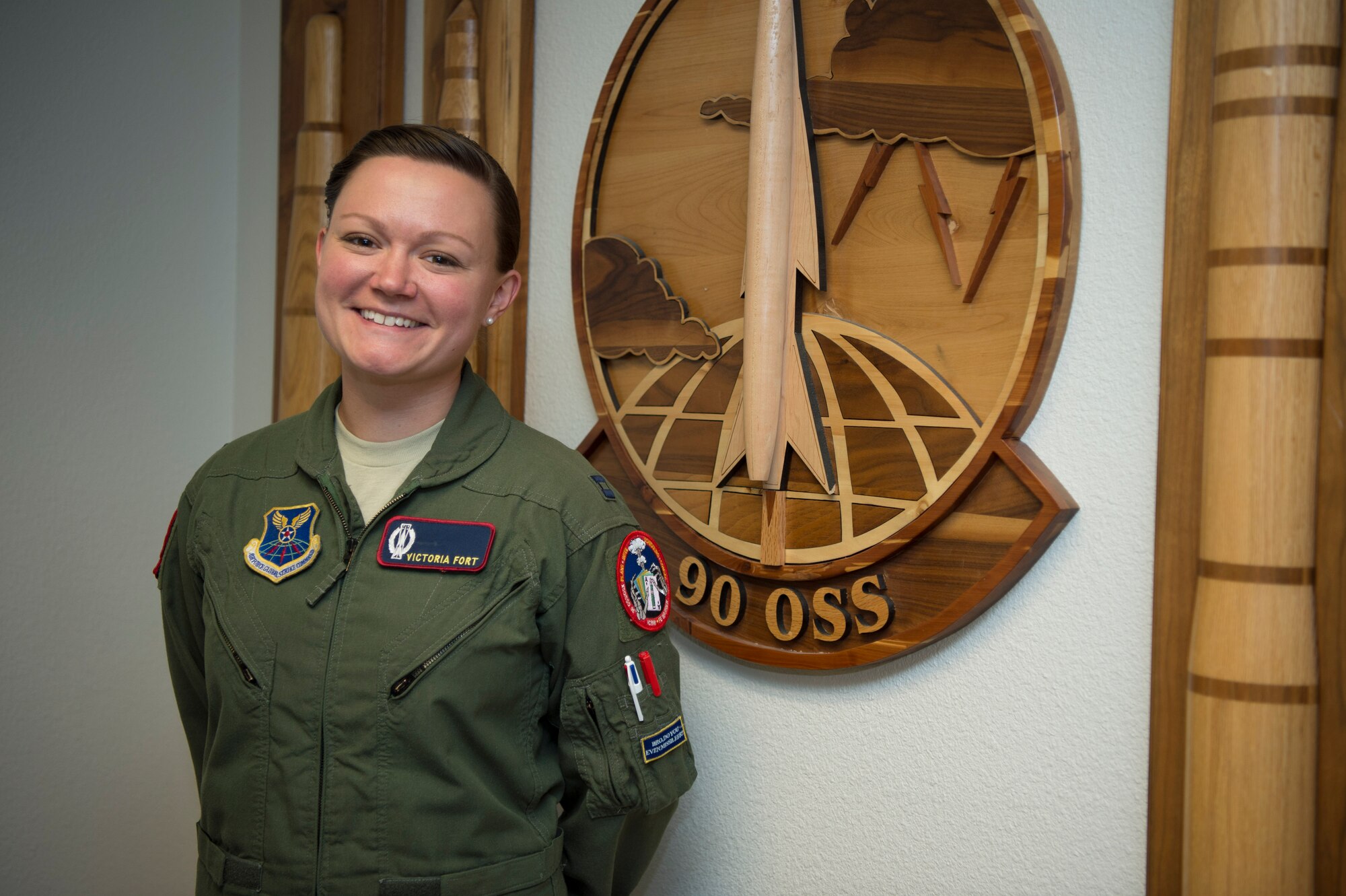 Capt. Victoria Fort, 90th Operational Support Squadron ICBM emergency war order planner, poses for a photo in front of the 90th OSS patch at F.E. Warren Air Force Base, Wyo., Sept. 20, 2016. The 90th OSS is part of the 90th Operations Group, which is charged with the control of 15 Missile Alert Facilities and 150 Minuteman III ICBMs in a 9,600 square mile area covering three states. (U.S. Air Force photo by Staff Sgt. Christopher Ruano)