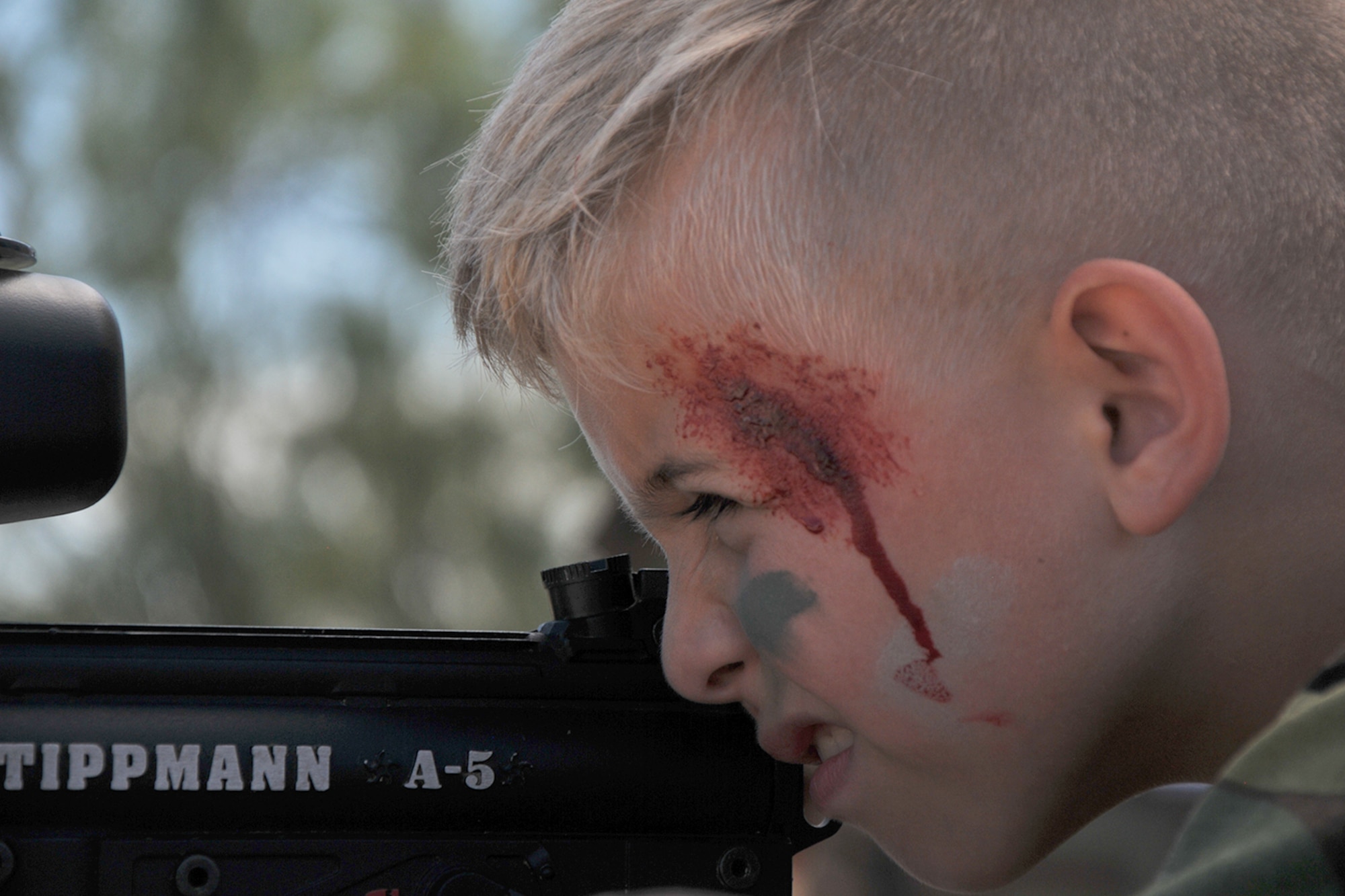 A child, wearing face-paint, fires a paint-ball gun during Operation Kids Investigating Deployment Services at Camp Sentinel on Goodfellow Air Force Base, Texas, Oct. 1, 2016. Operation KIDS volunteers taught the children how to aim and fire paint-ball guns. (U.S. Air Force photo by Airman 1st Class Randall Moose/Released)