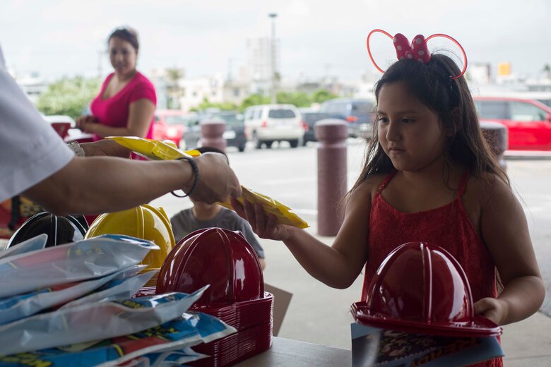 A child accepts gifts from the men and women with the Camp Foster Fire Department at the commissary on Camp Foster, Okinawa, Sept. 27, 2016. Emergency Awareness Day intends to increase the knowledge of the community by alerting people and providing them with a better understanding of the actions that need to be taken in the case of an emergency. (U.S. Marine Corps photo by MCIPAC Combat Camera Lance Cpl. Christian J. Robertson /Released)   