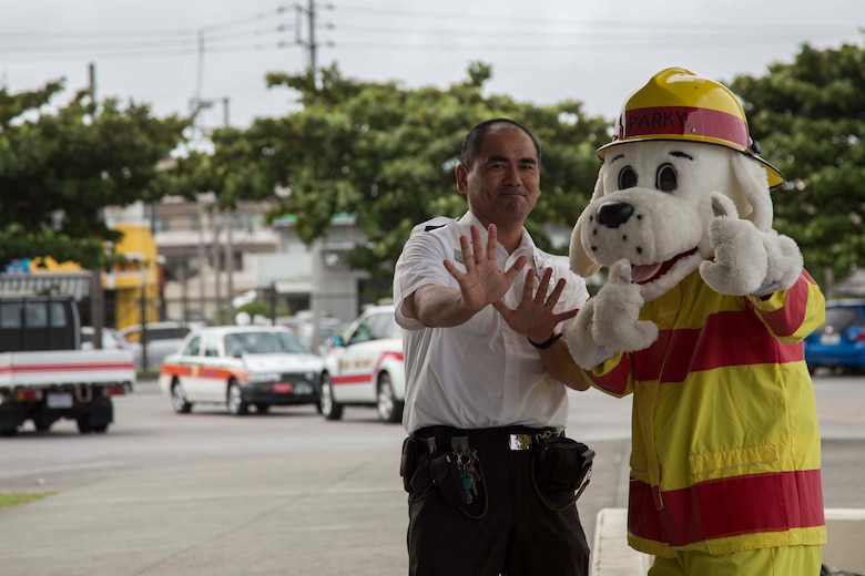 Sparky, a mascot with the Camp Foster Fire Department, poses with a Fire Inspector with the Camp Foster Fire Department at the commissary on Camp Foster, Okinawa, Sept. 27, 2016. Emergency Awareness Day intends to increase the knowledge of the community by alerting people and providing them with a better understanding of the actions that need to be taken in the case of an emergency. (U.S. Marine Corps photo by MCIPAC Combat Camera Lance Cpl. Christian J. Robertson /Released) 