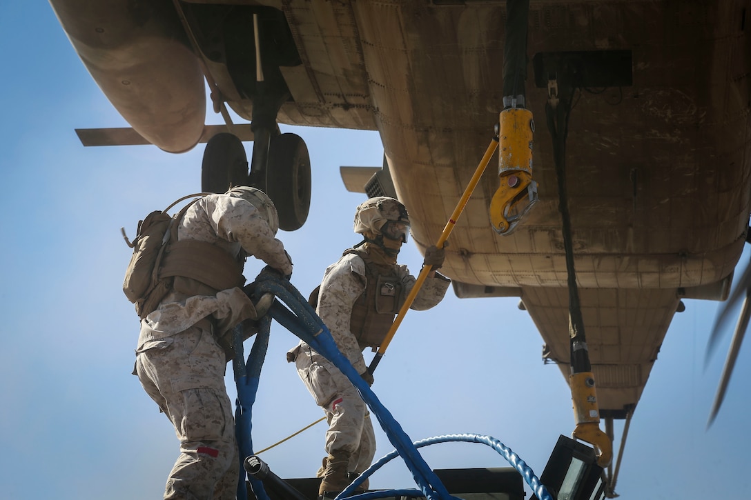 A Marine holds a static discharge rod against the cargo hook of a CH-53E Super Stallion helicopter as a second Marine prepares to hook up a set of sling ropes connected to a light armored vehicle during a slingload tactics exercise at Auxiliary Airfield II, Yuma, Ariz., Sept. 30, 2016. Marine Corps photo by Staff Sgt. Artur Shvartsberg