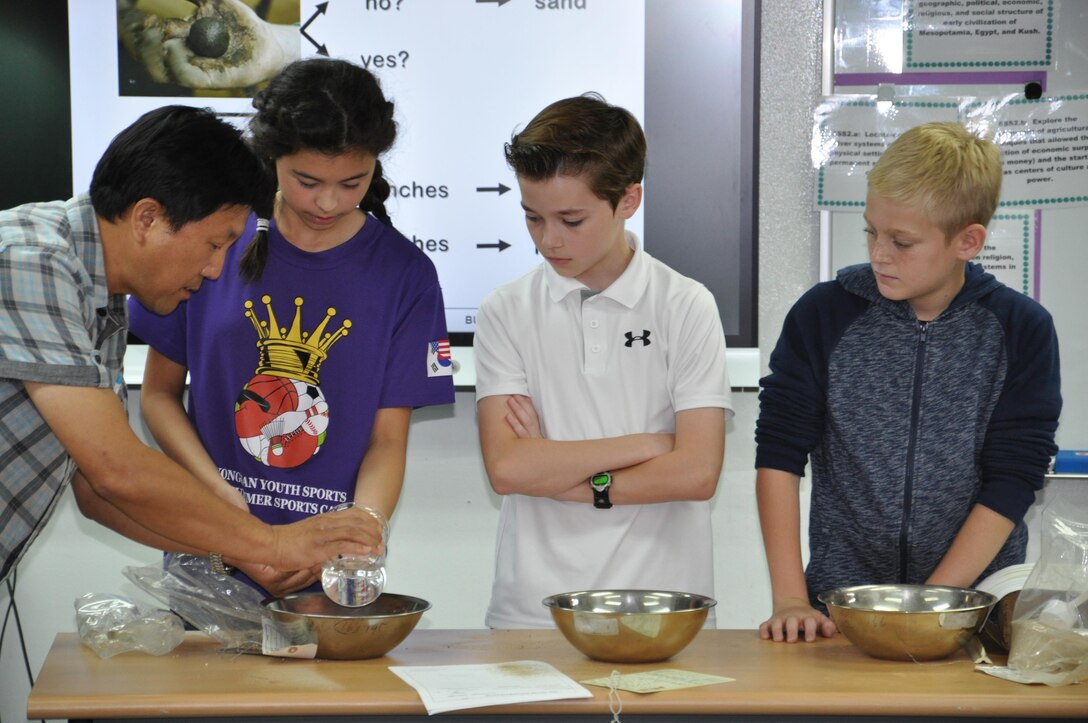 Kwon, Ku-hyon, Far East District geotechnical engineer, helps Seoul American Elementary School sixth-grade students Sarah Burton, Gage Hatalosky and Oden Kickhofel during a soil permeability experiment Sept. 30 at Seoul American Elementary School.