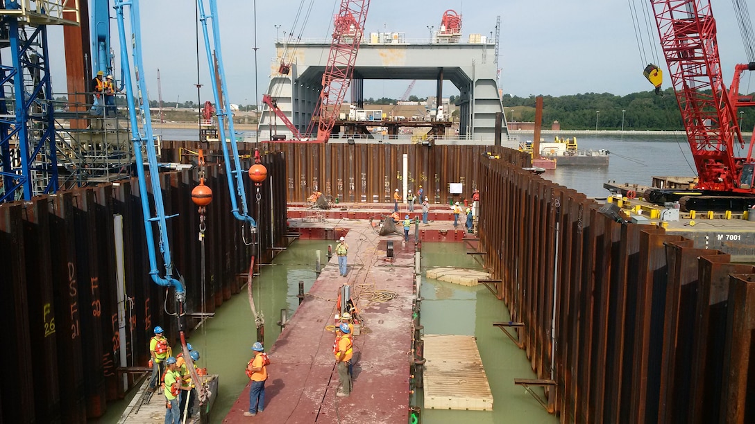 A tremie concrete mat is placed in the Left Boat Abutment while Navigable Pass Shell No. 9 is being set in the background. The Dam construction project is on the lower Ohio River.
