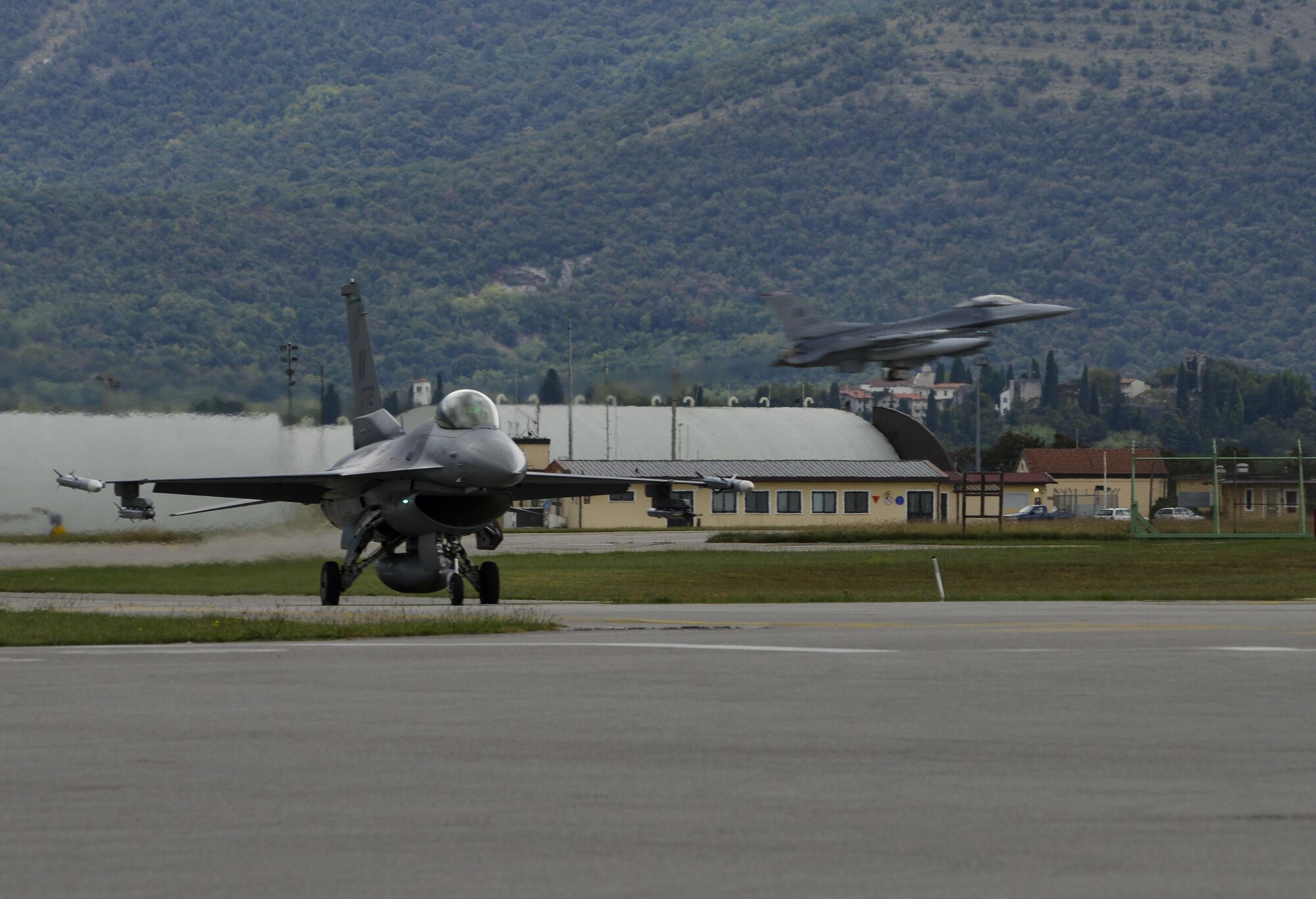A 555th Fighter Squadron F-16 Fighting Falcon taxis across the runway while a 510th Fighter Squadron F-16 lands at Aviano Air Base, Italy on Oct. 5, 2016. The two squadron’s frequently train to ensure the 31st Fighter Wing is ready to deliver combat air power and support across the globe. (U.S. Air Force photo by Senior Airman Krystal Ardrey/Released)