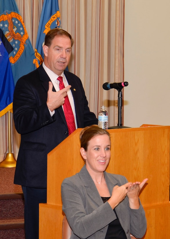 DLA Disposition Services Director Mike Cannon gives his opening remarks during the Hart-Dole-Inouye Federal Center's People With Disabilities program while Renelle Hansen interprets his remarks for deaf or hard of hearing audience members. 