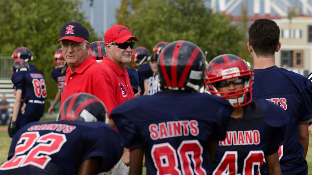 Coaches Ken McNeely and Andrew Dahlstrom talk to football players during their homecoming game at Aviano Air Base, Italy on Oct. 1, 2016. McNeely and Dahlstrom have been the only head coaches since the team’s inception in 1974. (U.S. Air Force photo by Airman 1st Class Cary Smith/Released)