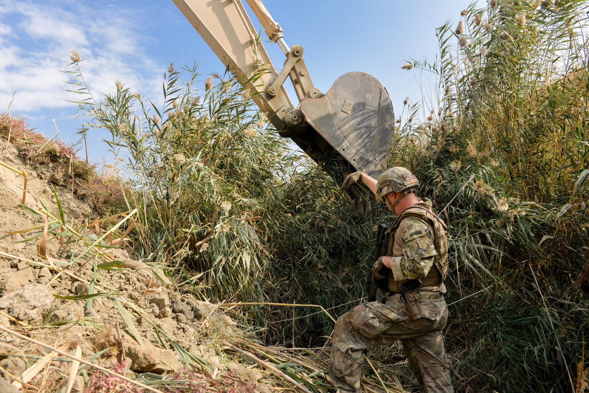 Capt. Erik Blum, Train, Advise, Assist Command-Air (TAAC-Air) civil engineer advisor, directs an excavator from a trench during a field clearing mission at Kabul Air Wing, Afghanistan, Oct. 6, 2016. Civil engineer advisors took on the project to clear a field of reeds that had grown to an excess of 15 feet, preventing security forces members manning an entry control point from being able to properly view the surrounding area. 