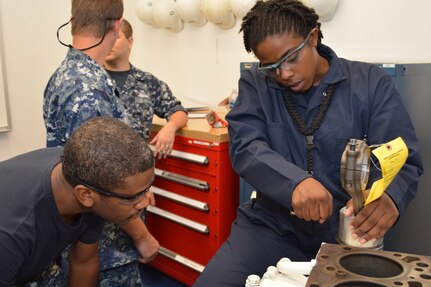 Petty Officer 1st Class Staci Allen explains how to remove an oil ring from the piston of a Cummins Diesel engine to Petty Officer 2nd Class Brian Sutton. Enginemen in the SERMC Diesel Shop service and repair diesel internal combustion engines and return them to the fleet.