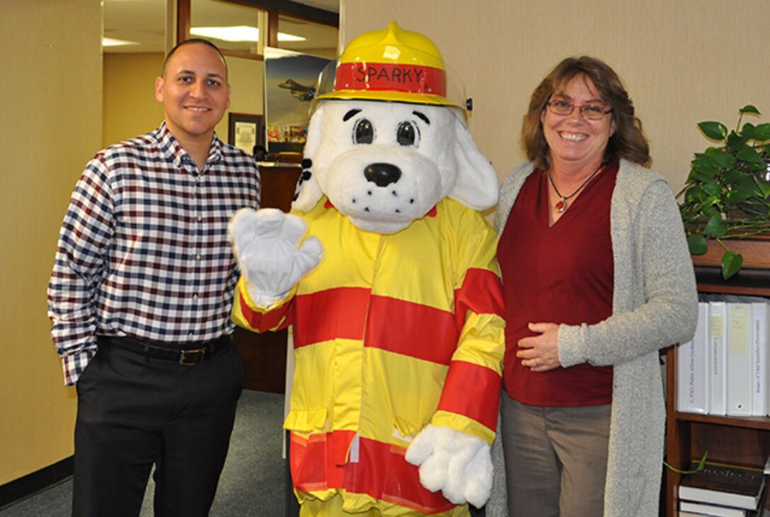 Sparky poses with Defense Logistics Agency Aviation Command Support Directorate employees, Maurice Sanabria, Command Programs Office chief; and Cathy Hopkins, public affairs specialist, while visiting offices on Defense Supply Center Richmond, Virginia, Oct. 11 to spread the word to check smoke alarms during Fire Prevention Week, Oct. 9-15, 2016.
