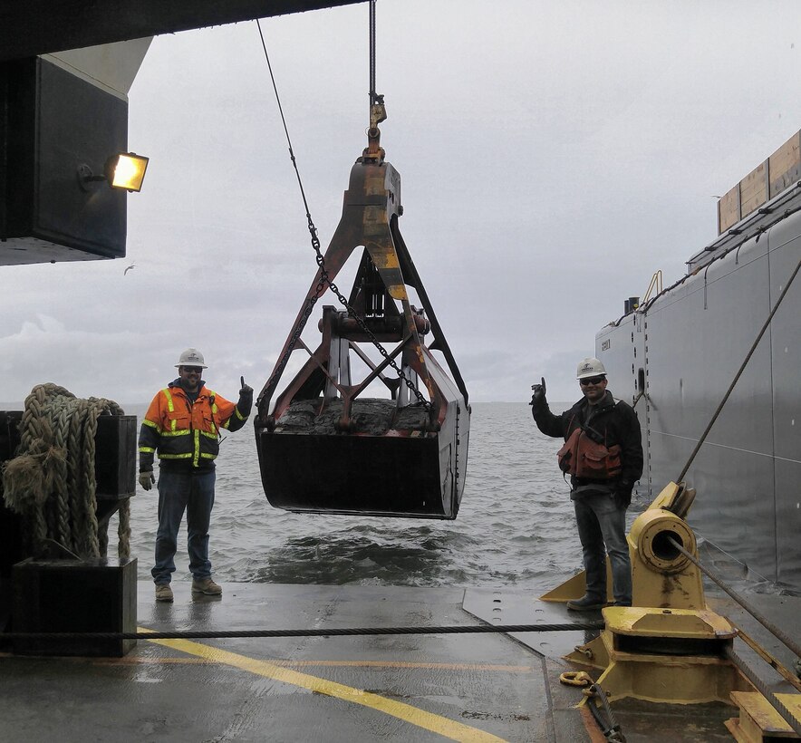 Maintenance and deepening dredging of the inner harbor at Grays Harbor has begun. The first bucket of dredged material pictured here, a 35-cubic-yard rehandling bucket, is flanked by American Construction's Aaron McMahill and Chris Raymond.