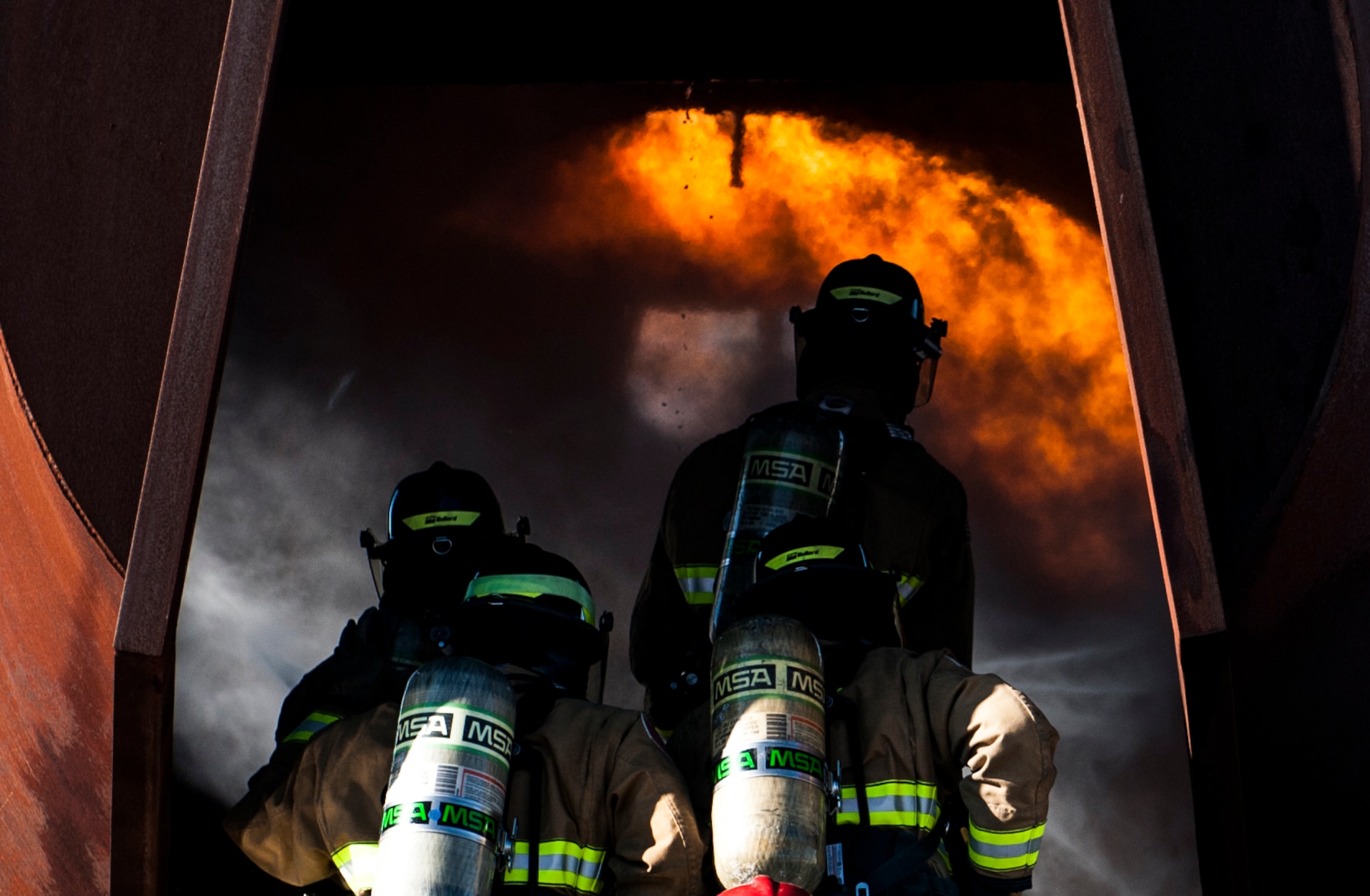 Firefighters, assigned to the 99th Civil Engineer Squadron Fire Protection Flight, enter the mock shell of an aircraft to perform controlled burn training at Nellis Air Force Base, Nev., Oct. 6, 2016. The NCFD will be hosting an Open House at Fire Station 1 on Nellis AFB, where they will be giving tours of the fire station to anyone that stops in. (U.S. Air Force photo by Airman 1st Class Kevin Tanenbaum/Released)