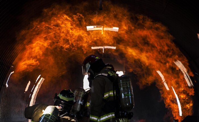 Jason Martinez, 99th Civil Engineer Squadron Fire Protection Flight firefighter, stands in the mock shell of an aircraft while performing controlled burn training at Nellis Air Force Base, Nev., Oct. 6, 2016. The Nellis-Creech Fire Department will be hosting events throughout the week to educate and bring awareness to the importance of fire safety. (U.S. Air Force photo by Airman 1st Class Kevin Tanenbaum/Released)