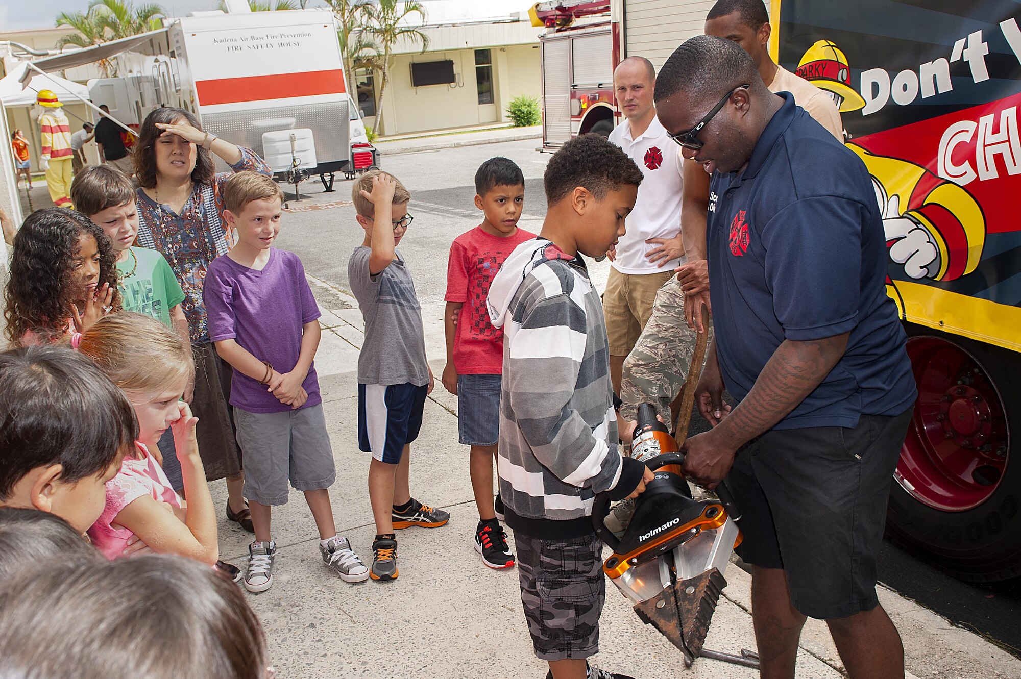 U.S. Air Force Staff Sgt. Demarcus Oliver, 18th Civil Engineer Squadron firefighter, shows children firefighting equipment during fire prevention week Oct. 5, 2016, at Kadena Air Base, Japan. During fire prevention week, 18th CES firefighters teach children fire safety tips, how to check smoke alarms and cap it off with a parade through the housing areas. (U.S. Air Force photo by Airman 1st Class Corey M. Pettis)